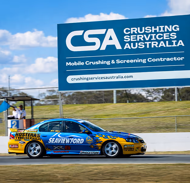 Black race car number 444 with neon yellow rims speeding on a racetrack under a blue sky with scattered clouds.