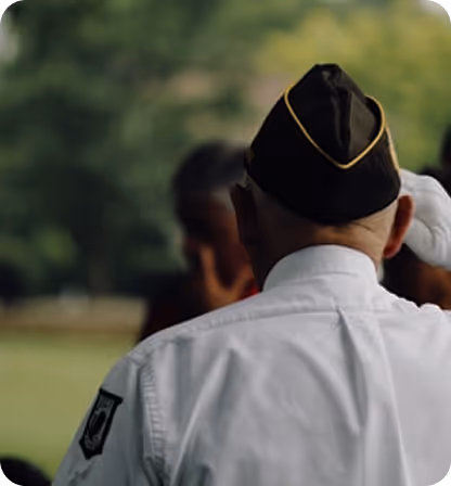Rear view of a veteran saluting outdoors wearing a white uniform and black cap with gold trim.