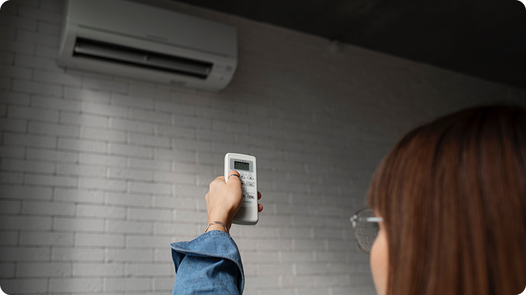 Person pointing a remote control at a wall-mounted air conditioner unit.