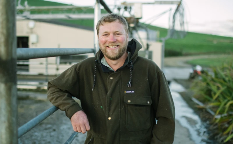 Grinning dairy farmer leans on the fence at the milking shed