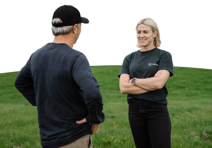 A woman wearing a Halter-branded shirt smiles while talking to a man in a cap on a grassy field.