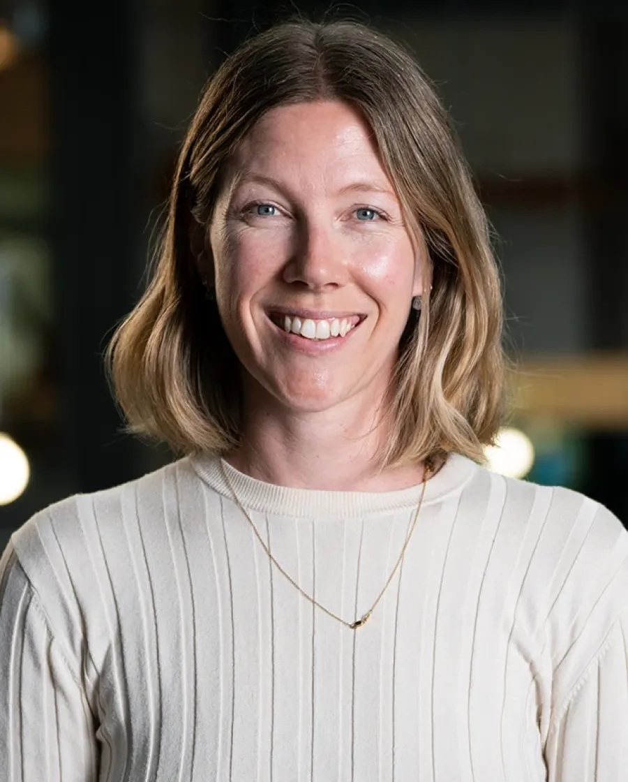 Portrait of Helen who is a smiling woman with shoulder-length blonde hair wearing a cream-colored ribbed sweater, photographed indoors.