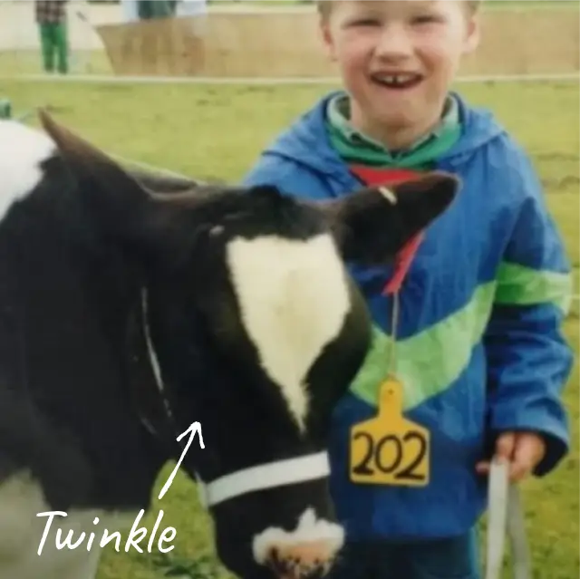 A young Craig Piggott stands smiling next to a black and white calf named Twinkle