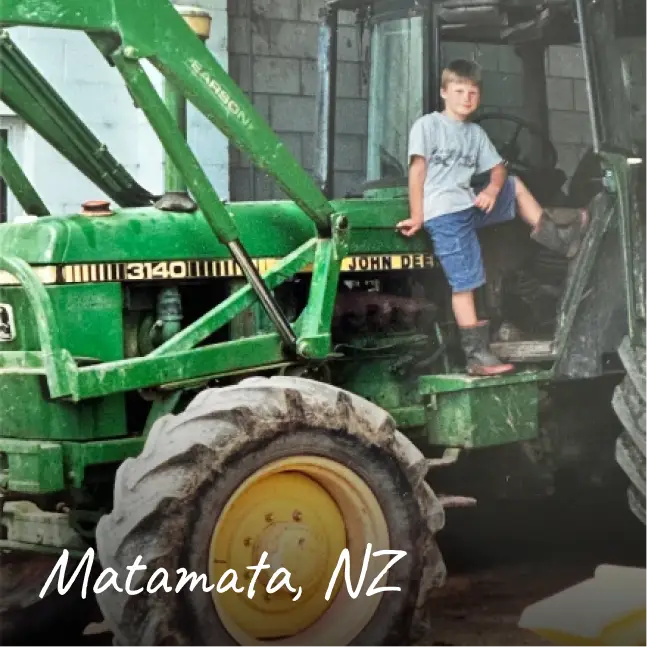 A young Craig Piggott poses proudly on the steps of a green tractor with “Matamata, NZ” written in the corner.