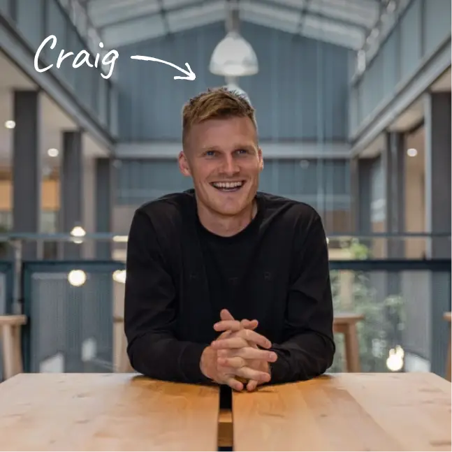 Craig Piggott, Halter founder & CEO, sits at a wooden table in a modern, industrial-style office, smiling with hands clasped.