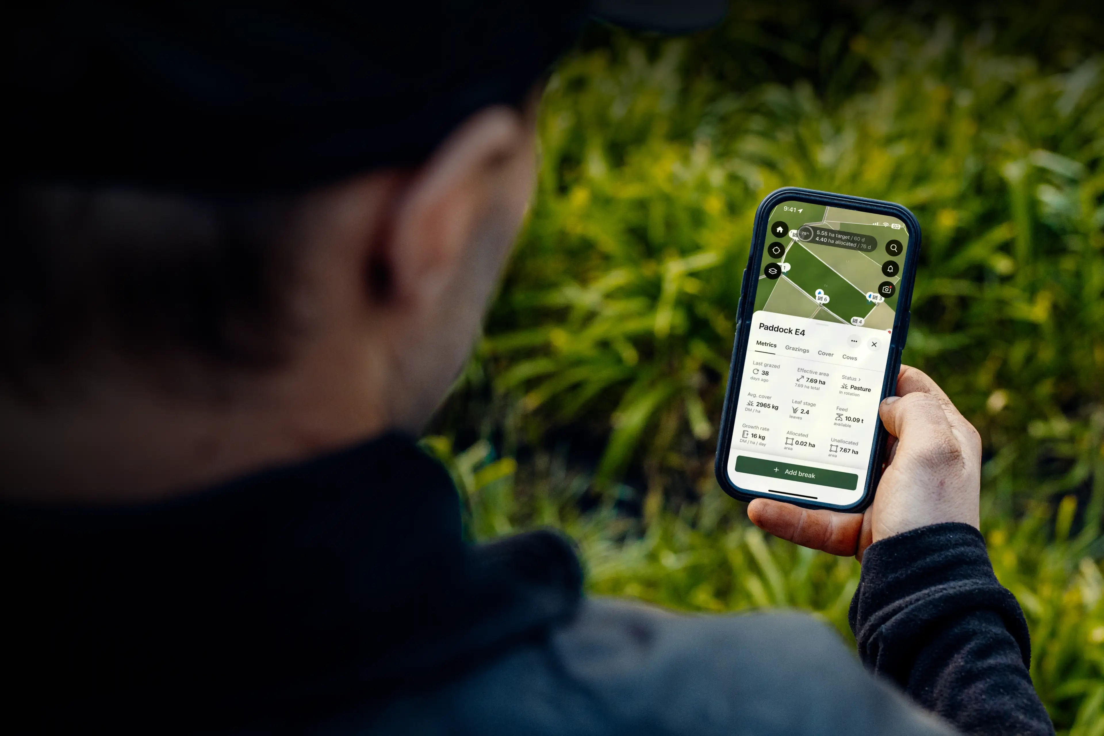 A person outdoors holds a smartphone displaying a satellite map and data dashboard for a paddock, part of the Halter app.