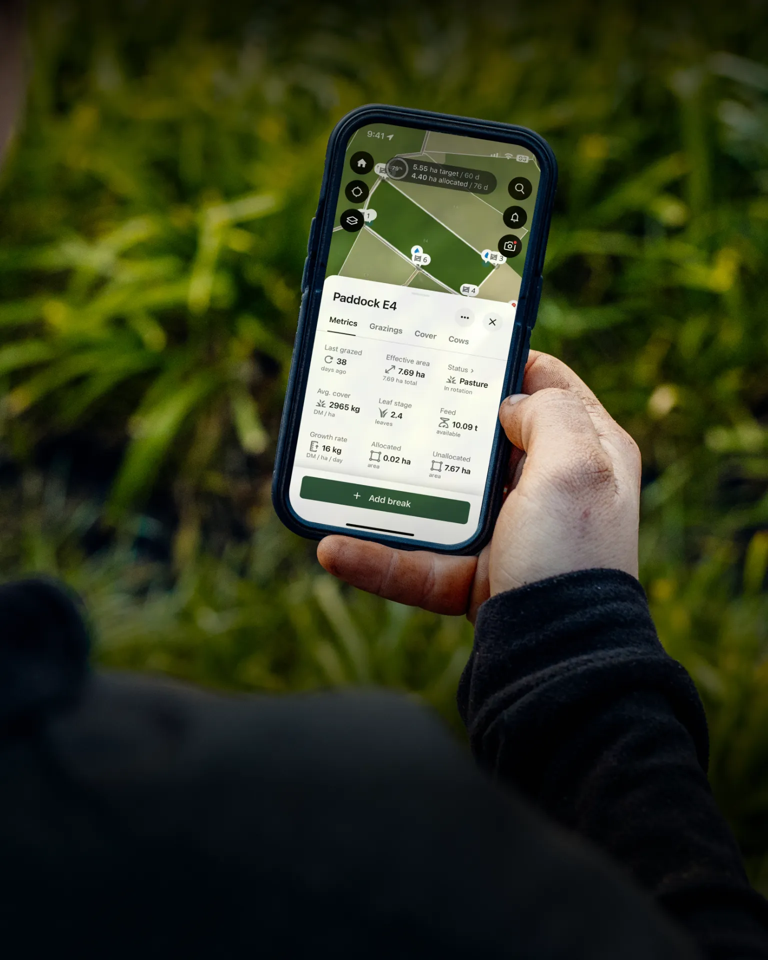 A person outdoors holds a smartphone displaying a satellite map and data dashboard for a paddock, part of the Halter app.