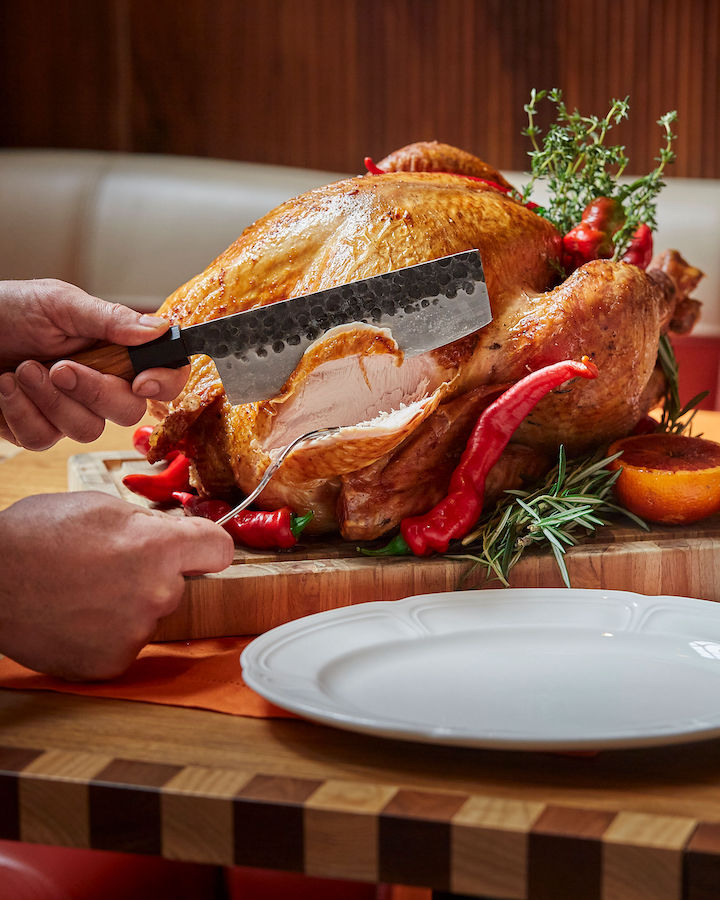 Photograph of a knife carving into a turkey for thanksgiving day.