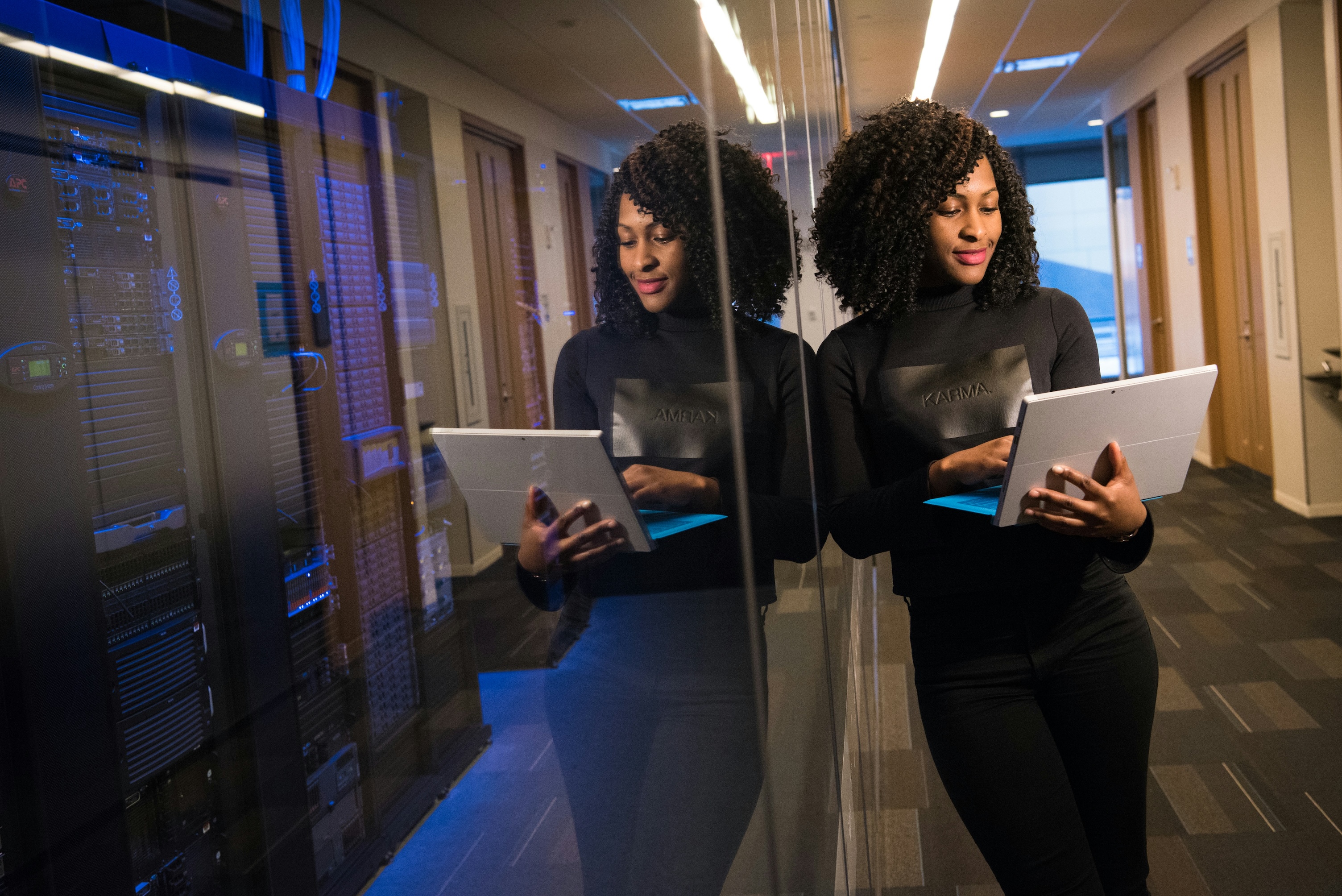 woman leaning on glass wall, working on laptop