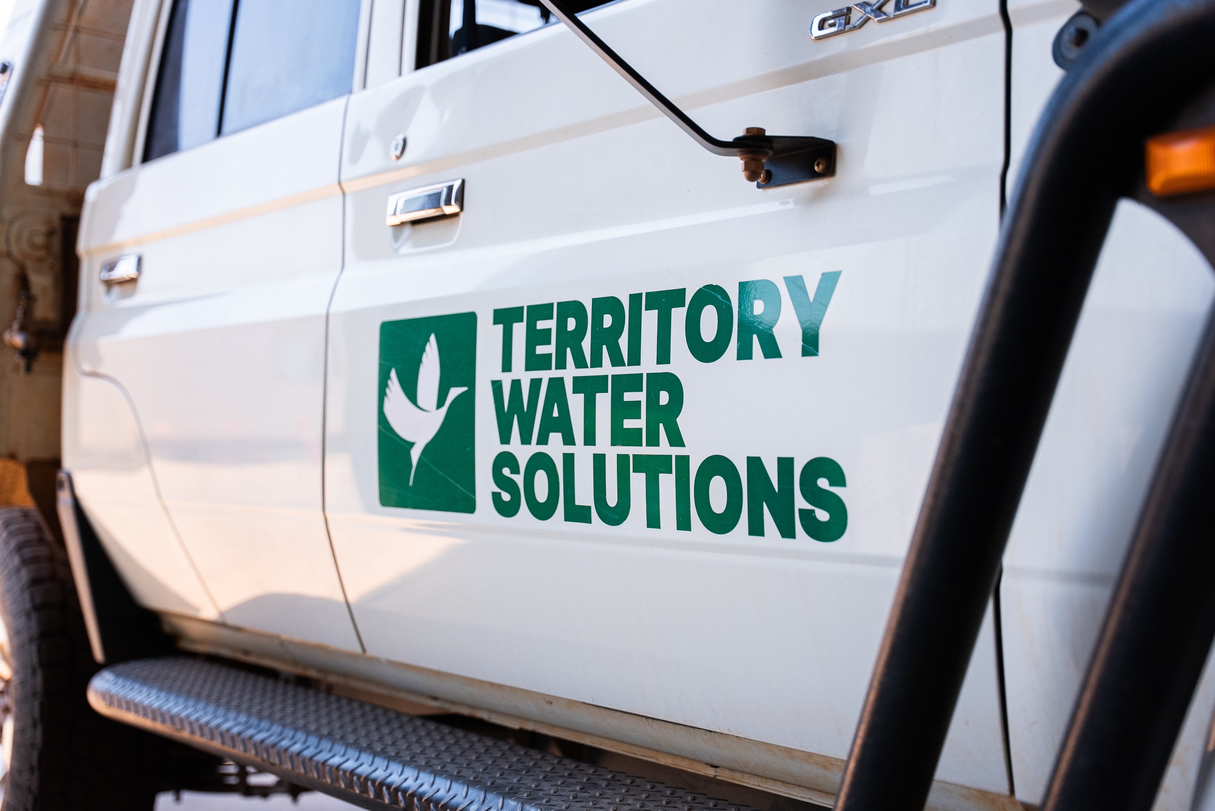 White vehicle door with green logo and text reading ‘Territory Water Solutions’ featuring a stylized bird.