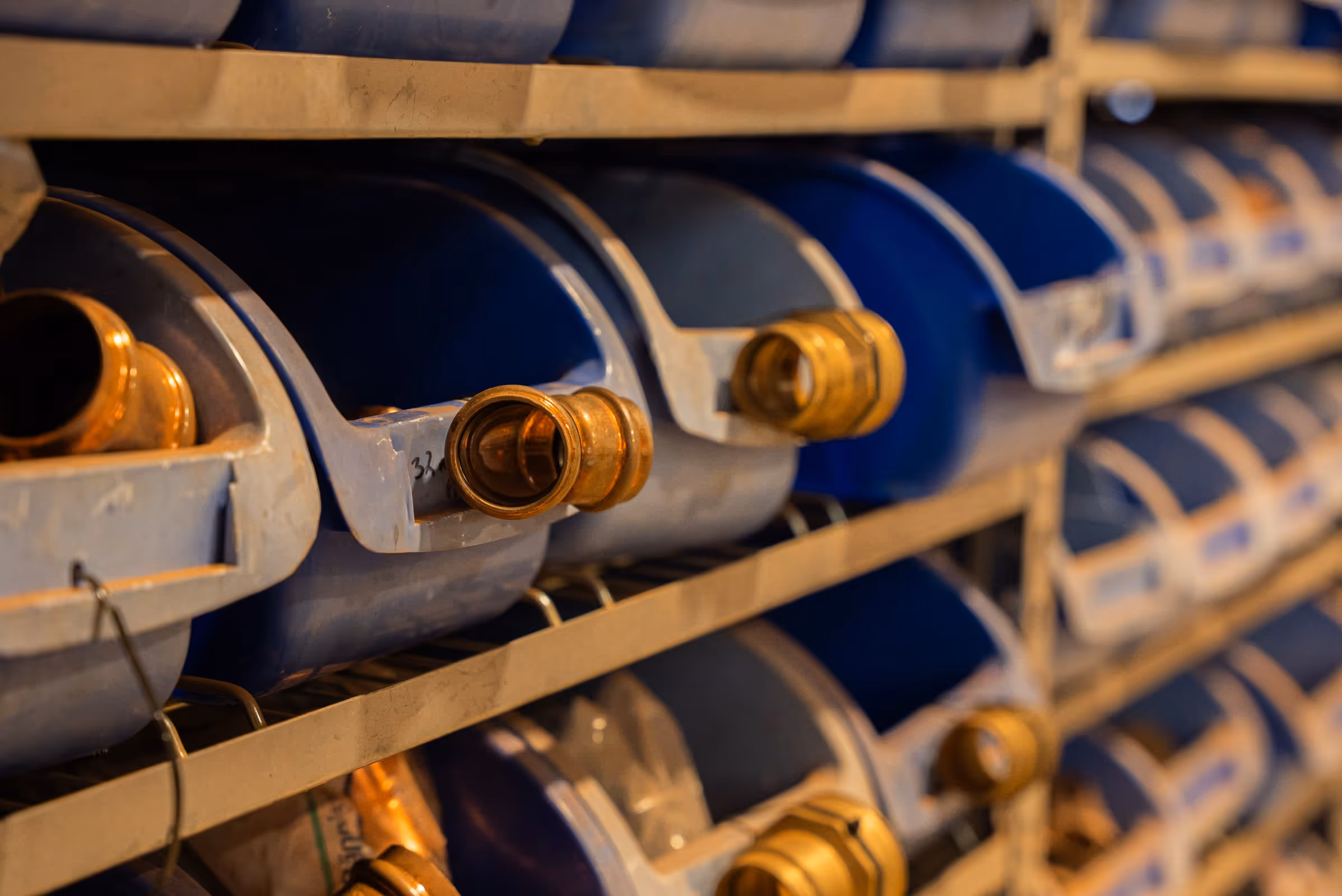 Rows of blue plastic containers with brass nozzles stored on beige metal shelves.