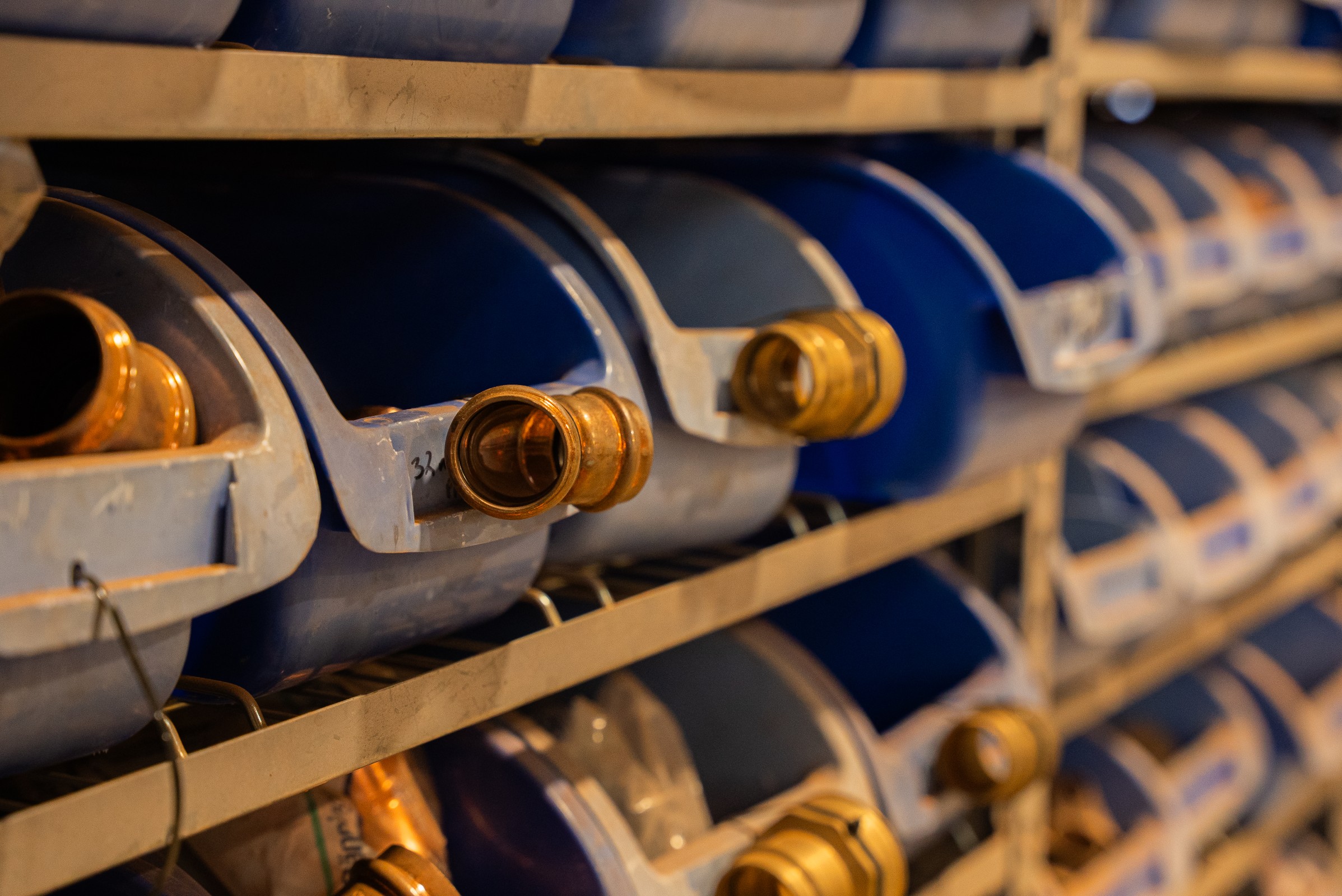 Rows of blue plastic containers with brass nozzles stored on beige metal shelves.