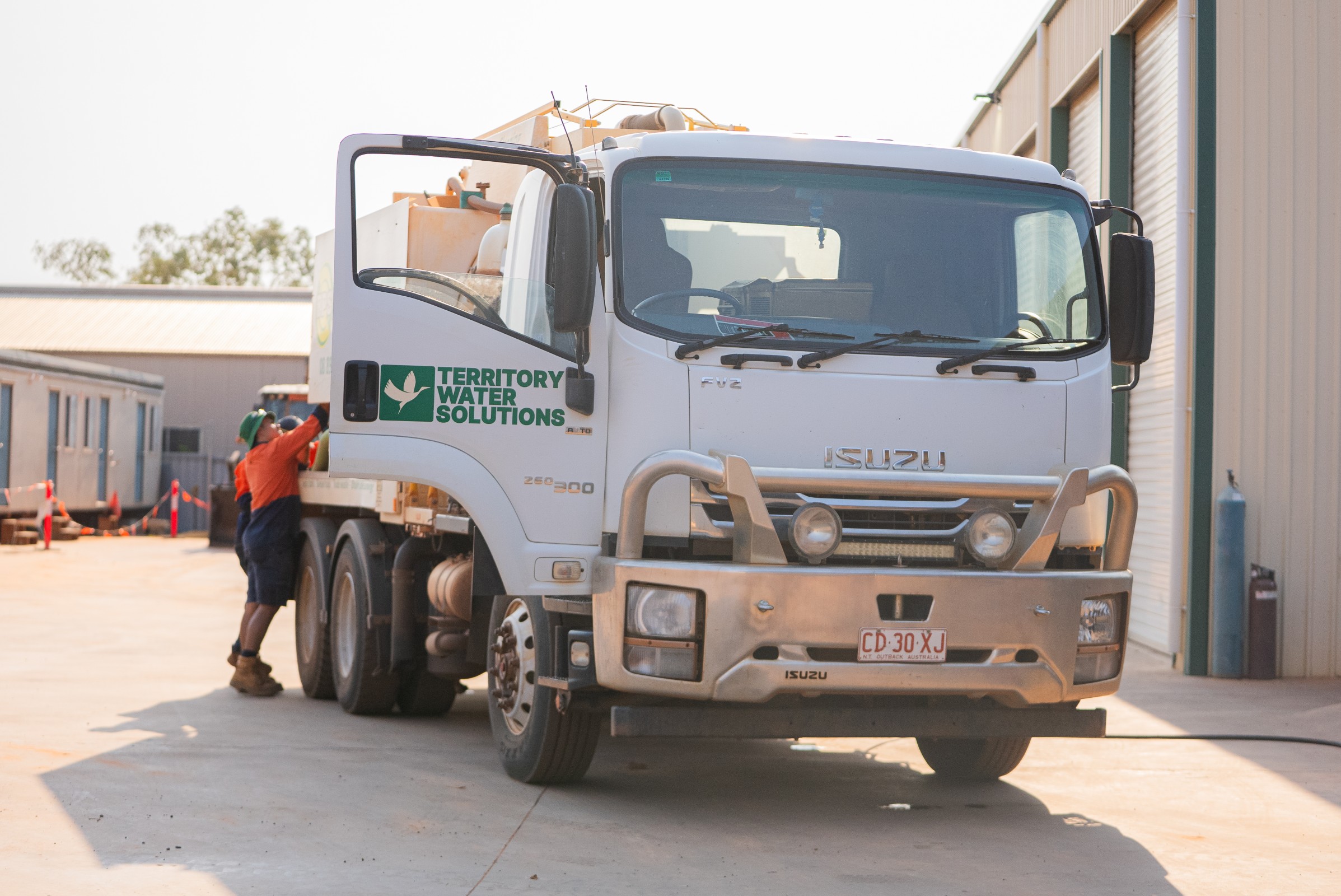 White Isuzu truck with Territory Water Solutions logo and worker in safety gear opening the driver's door.