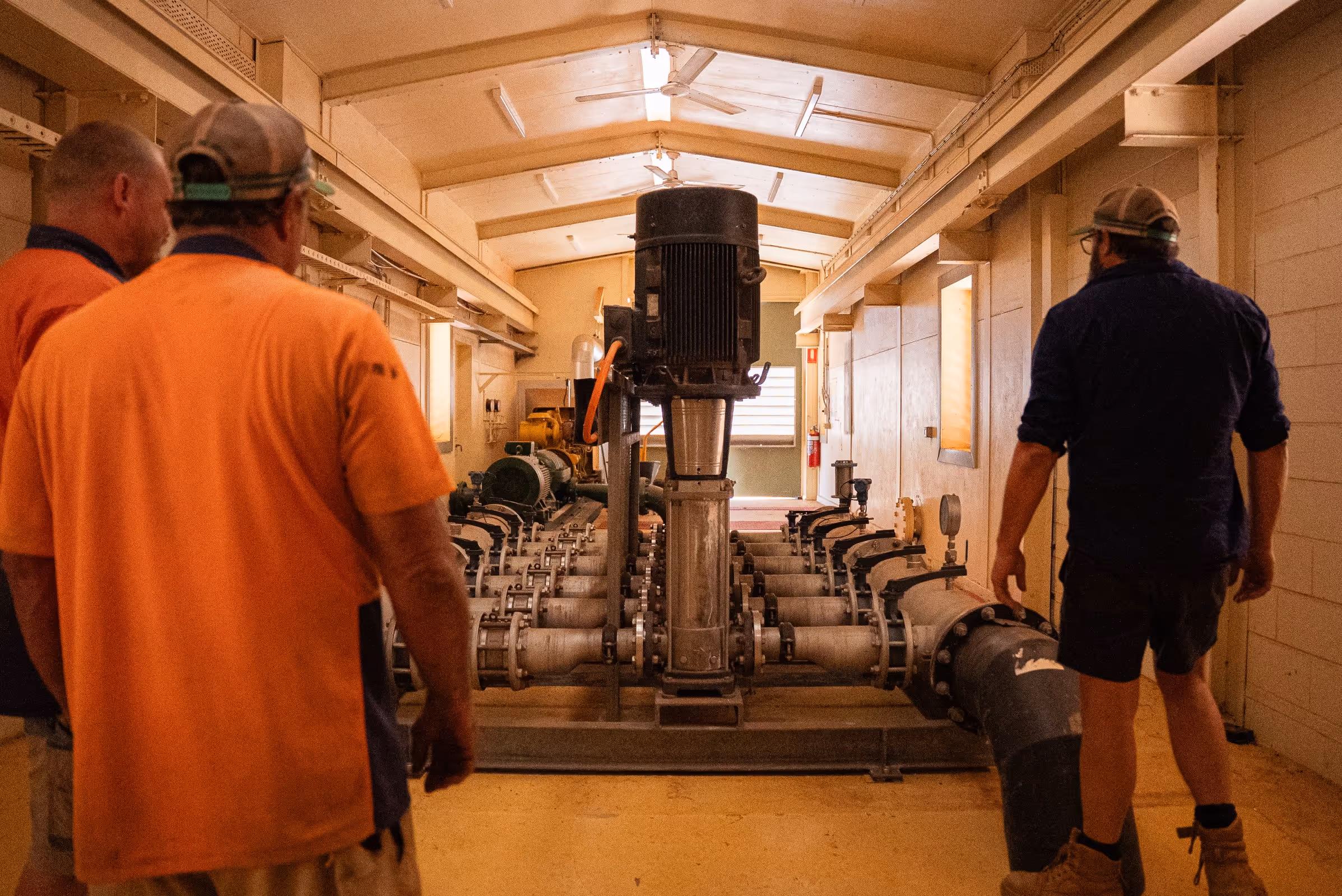 Three men in a utility room inspecting industrial water pump machinery with connected pipes.