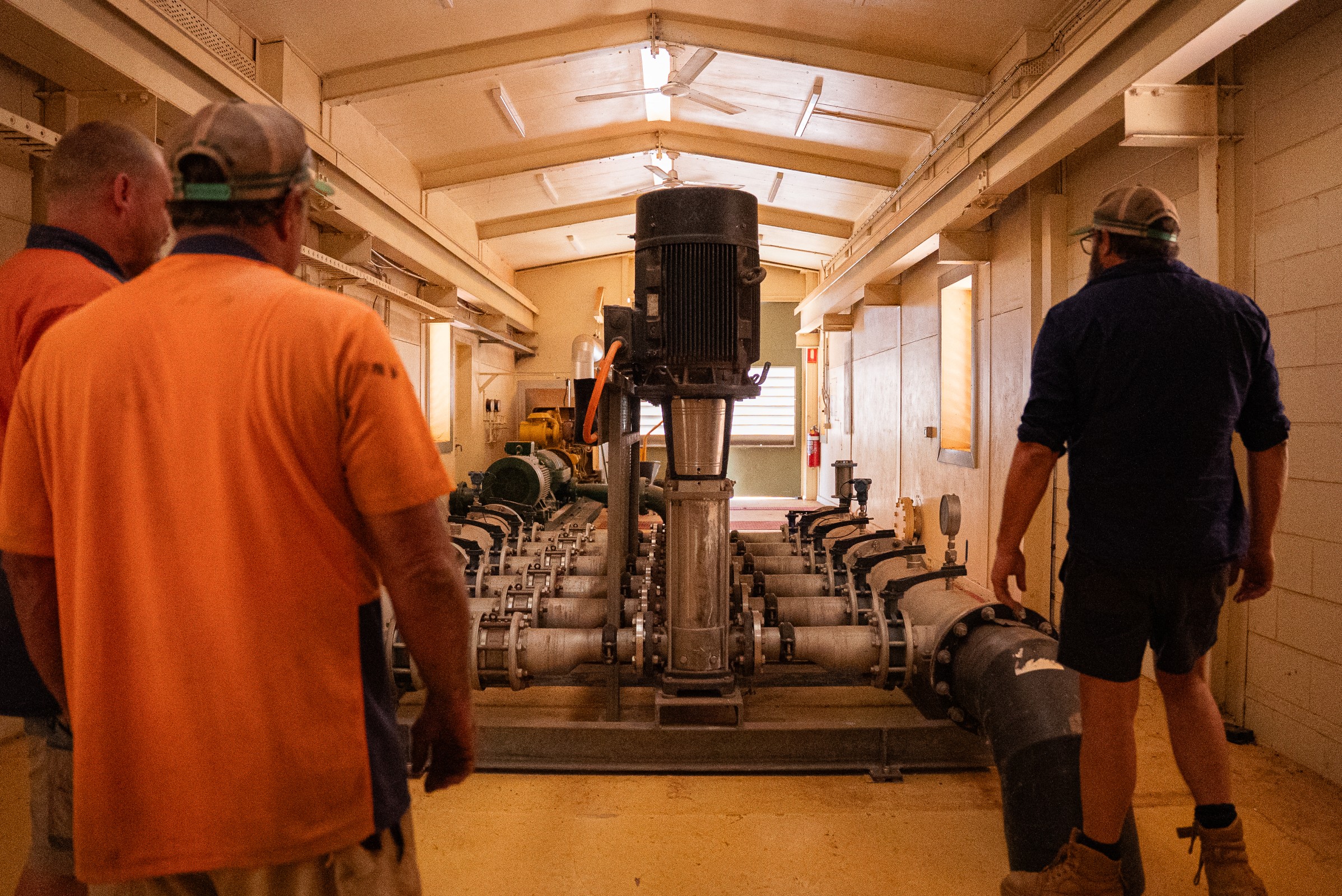 Three men in a utility room inspecting industrial water pump machinery with connected pipes.