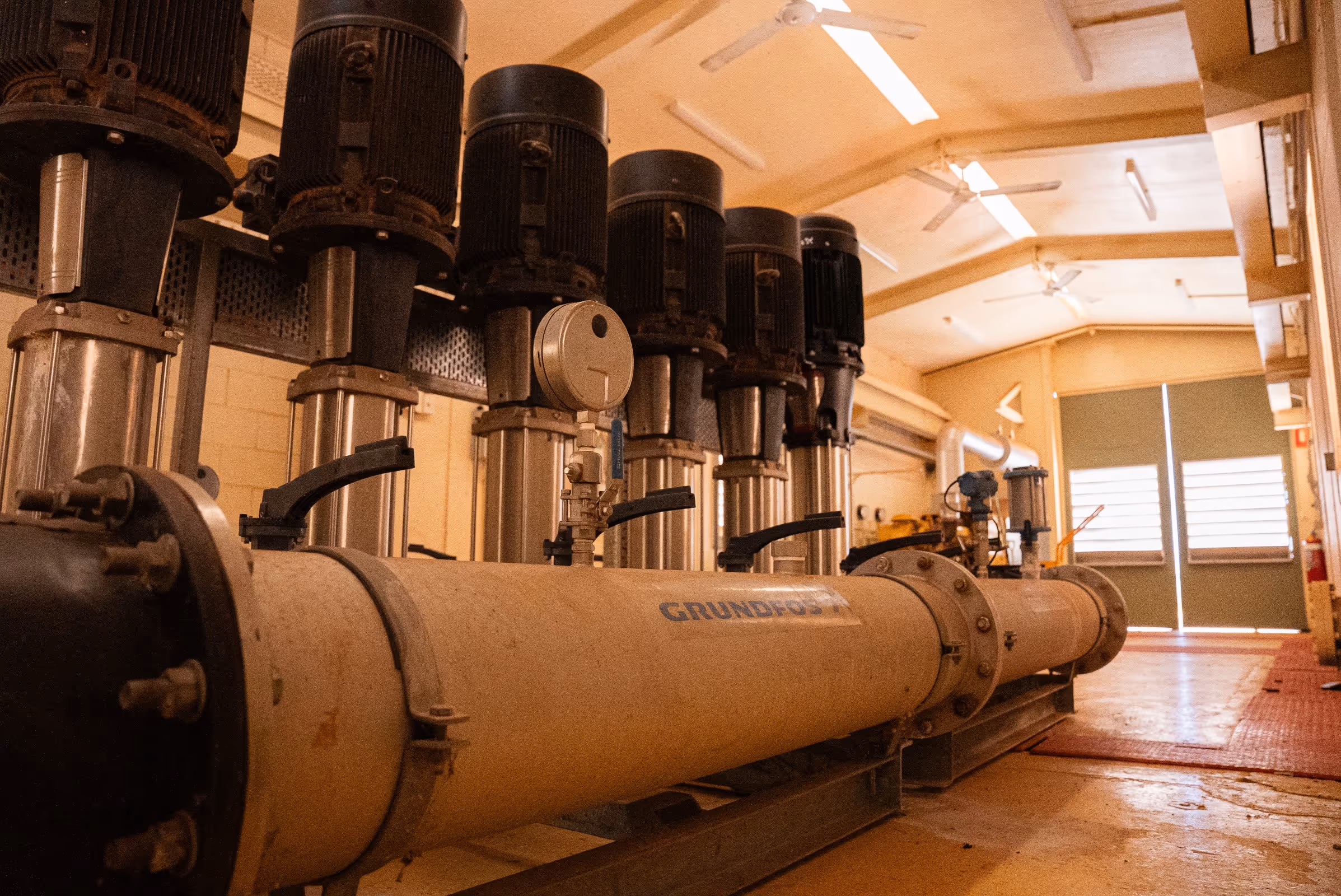 Industrial room with large Grundfos water pumps and pipes arranged in a row.