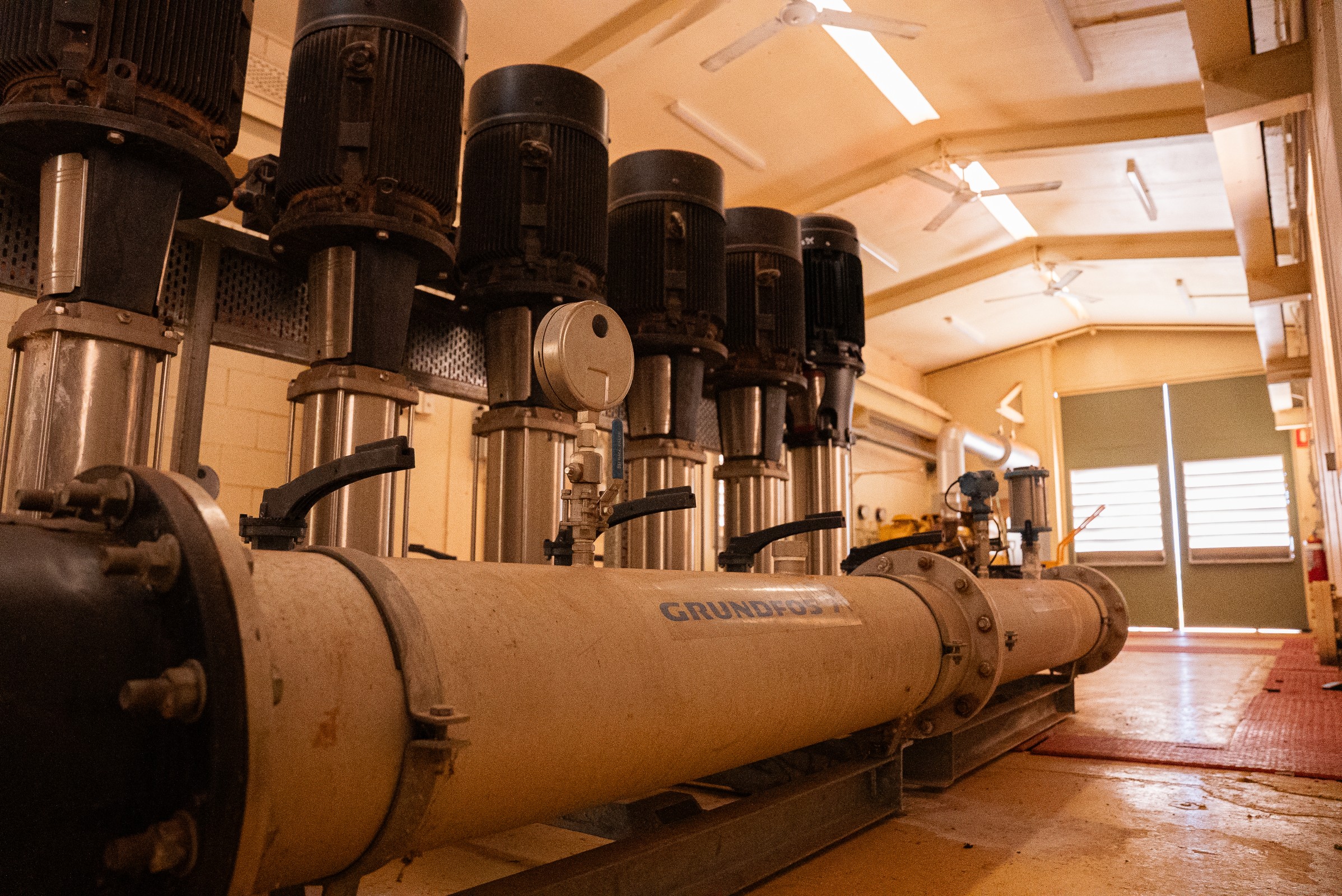 Industrial room with large Grundfos water pumps and pipes arranged in a row.