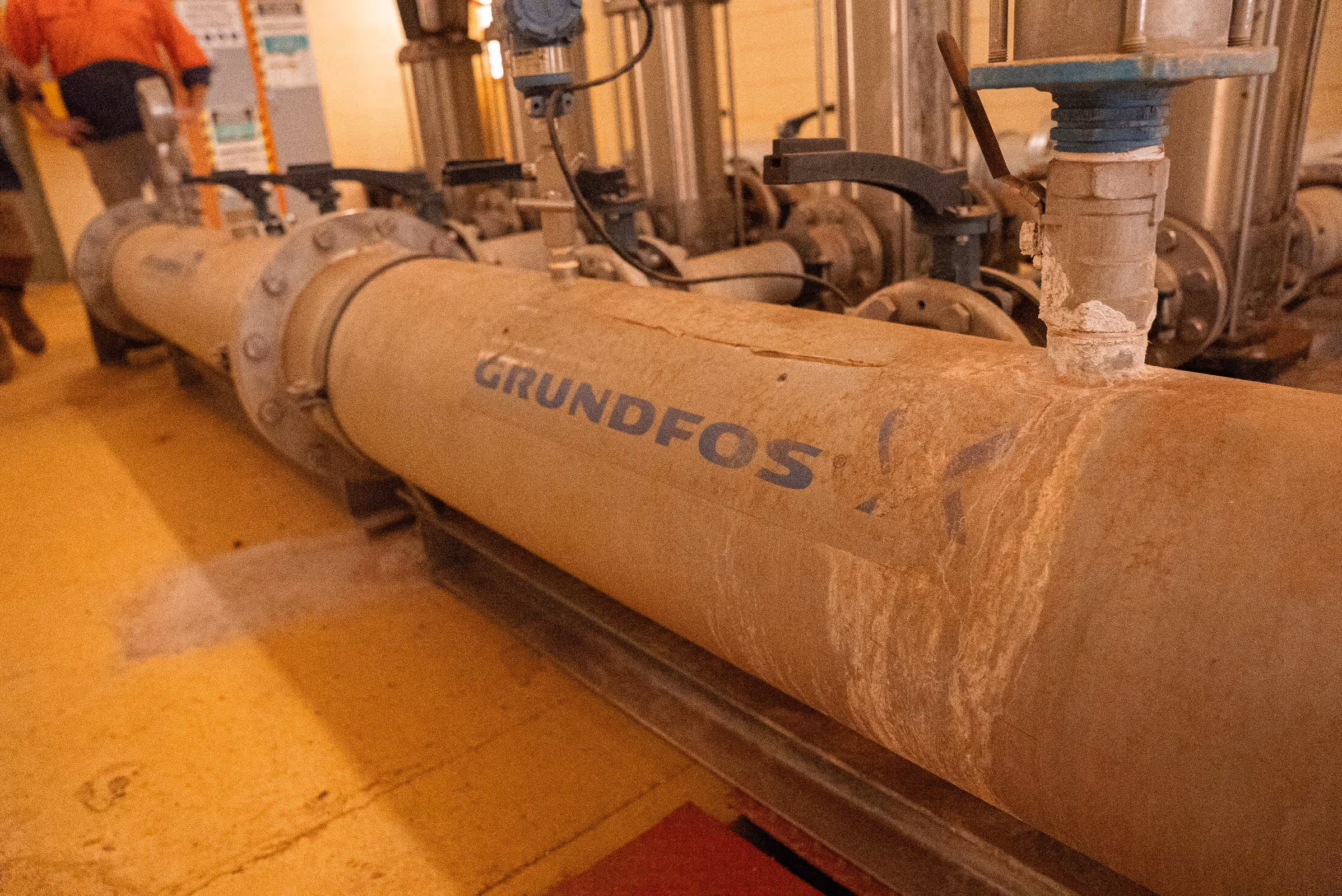 Rusty industrial pipe with the brand name GRUNDFOS in a mechanical room.