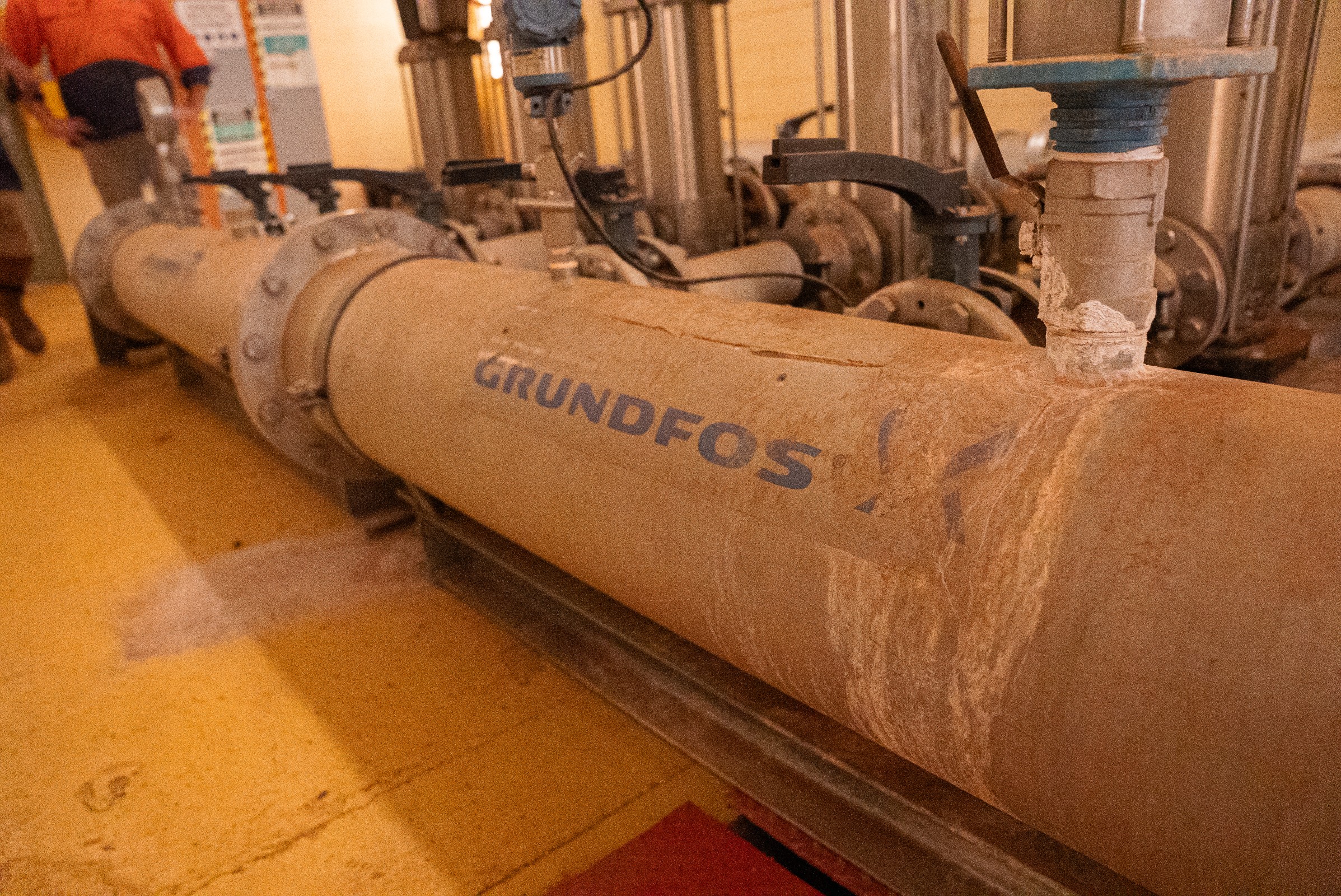 Rusty industrial pipe with the brand name GRUNDFOS in a mechanical room.