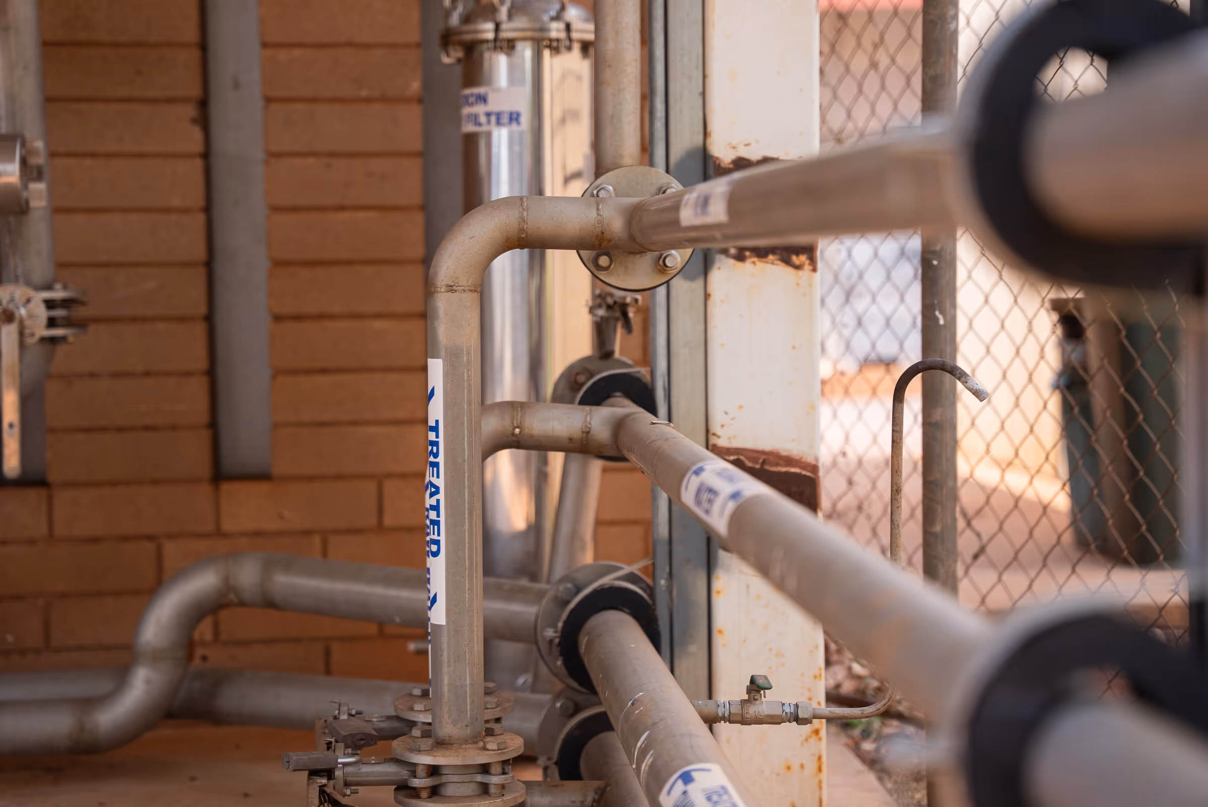 Close-up of industrial metal pipes labeled 'TREATMENT' with valves and a brick wall background.