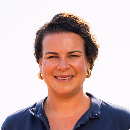 Portrait of a smiling woman with short curly hair wearing gold hoop earrings and a navy blue collared shirt.