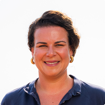 Portrait of a smiling woman with short curly hair wearing gold hoop earrings and a navy blue collared shirt.