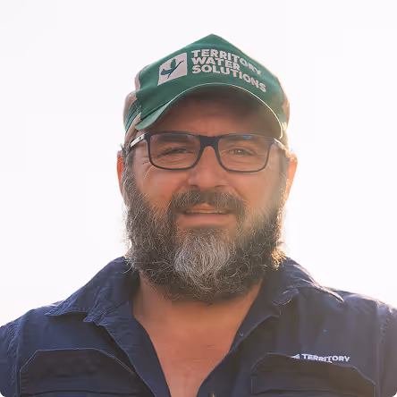 Bearded man wearing glasses and a green Territory Water Solutions cap, smiling in natural light.