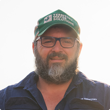 Bearded man wearing glasses and a green Territory Water Solutions cap, smiling in natural light.