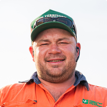 Smiling man wearing an orange work shirt and green cap with sunglasses resting on the cap.