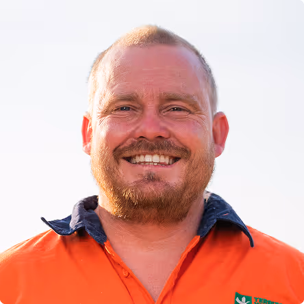 Smiling man with short hair and beard wearing an orange collared shirt with a navy collar.