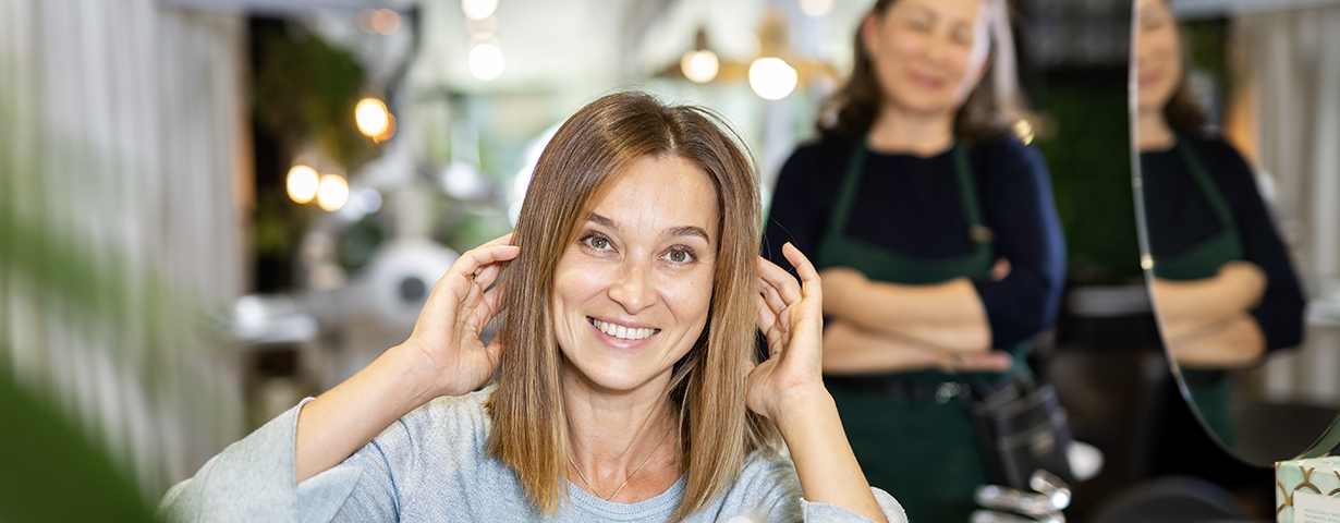 Smiling client touching her freshly styled hair in a salon mirror as her stylist looks on, reflecting Q2 2026 salon data