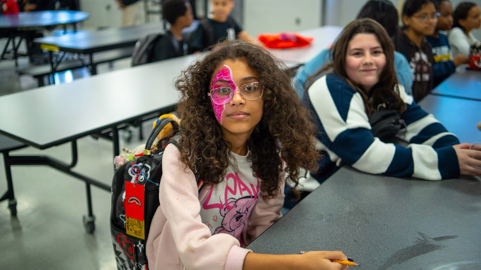 Student with pink spider-web face paint sitting at a cafeteria table