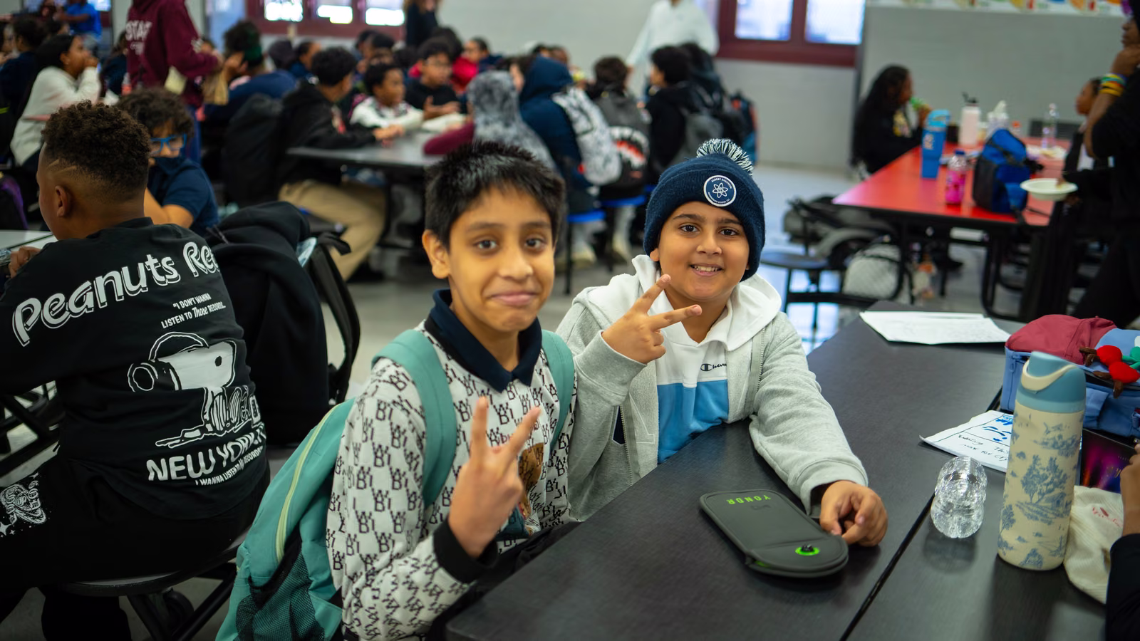 Two students smiling and making peace signs in the cafeteria