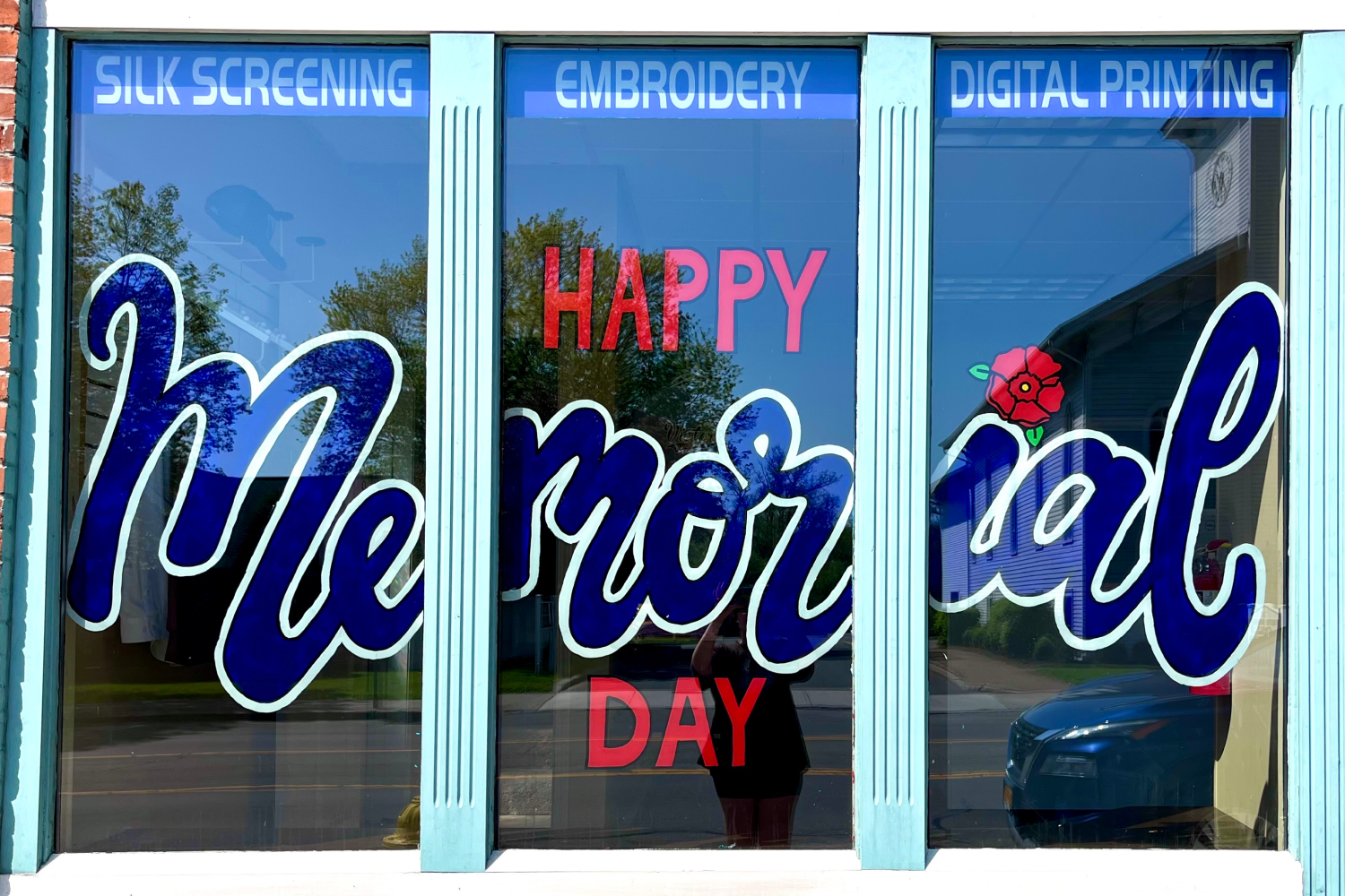 Window with a red poppy flower and the words "Happy Memorial Day" painted in blue and red cursive letters.