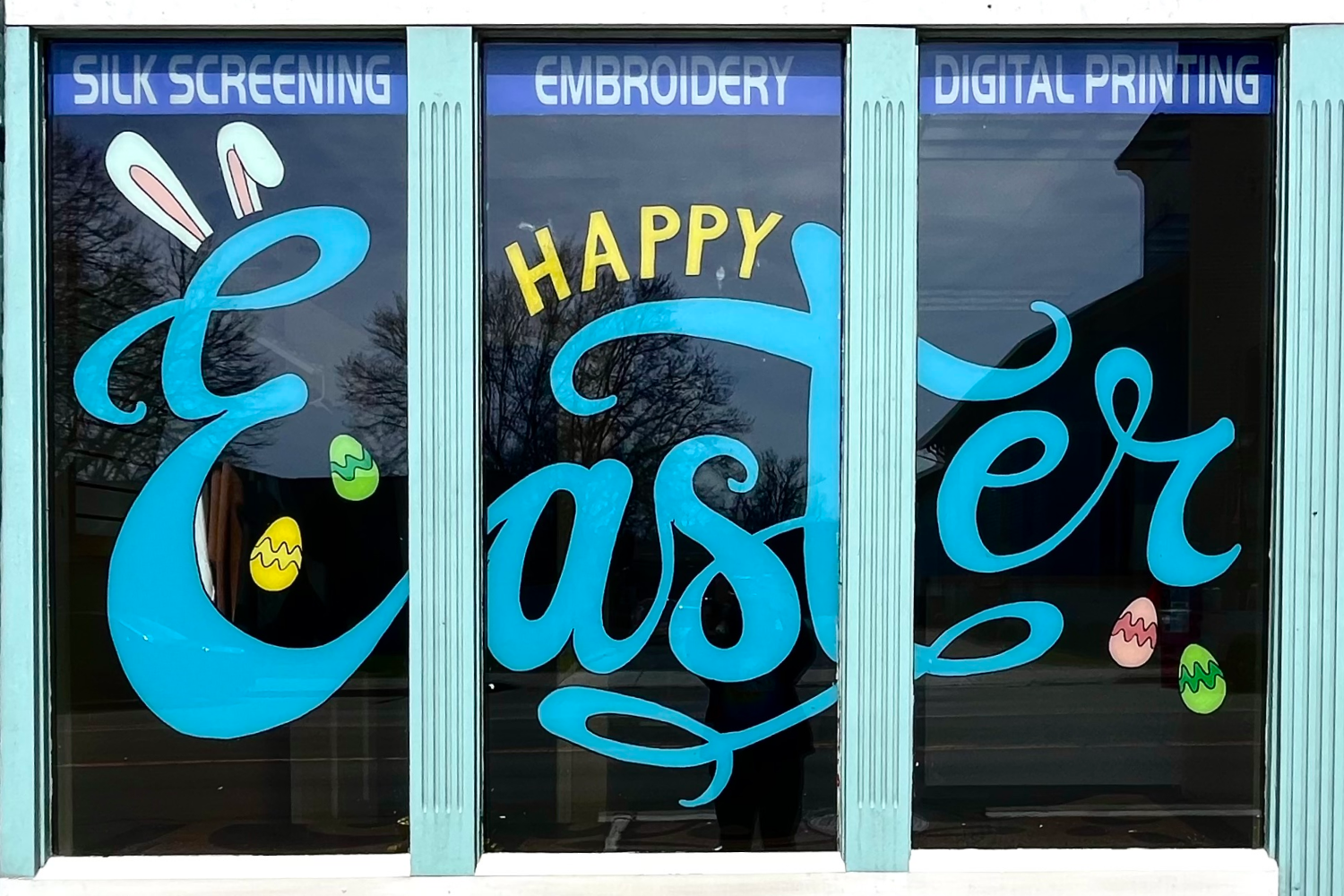 Window with little colorful easter eggs and the words "Happy Easter" painted in blue cursive letters.