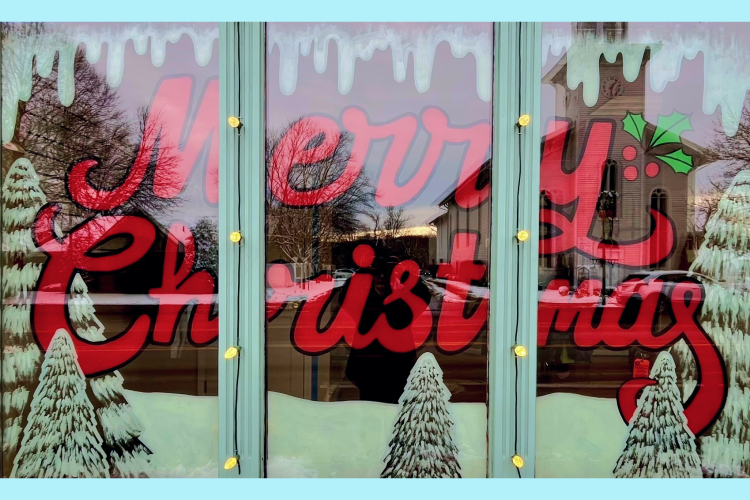 Window with white pine trees, snow, and the words "Merry Christmas" painted in red cursive letters.