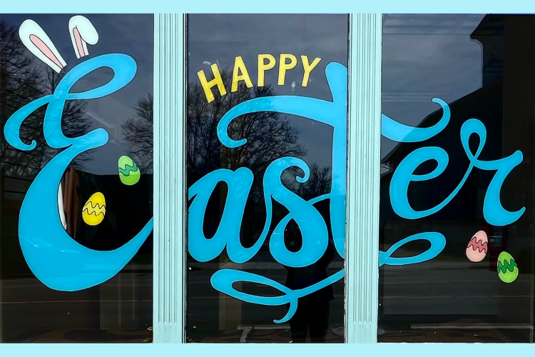 Window with little colorful easter eggs and the words "Happy Easter" painted in blue cursive letters.