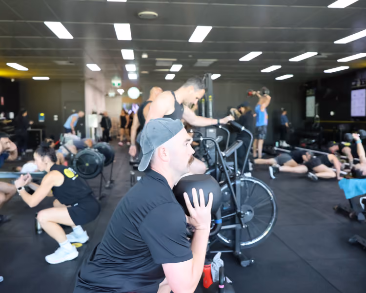 People exercising in a gym with equipment doing squats and weightlifting.