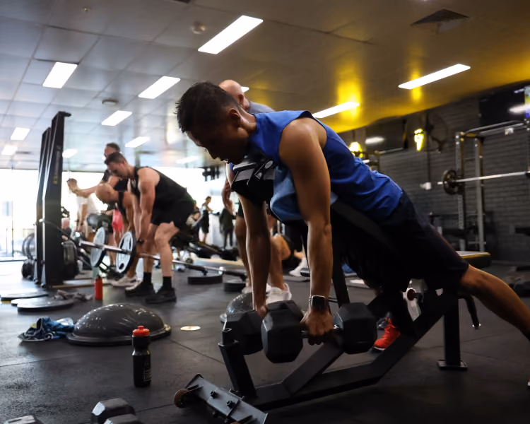 Man lifting dumbbells on an incline bench with others exercising in a gym setting.