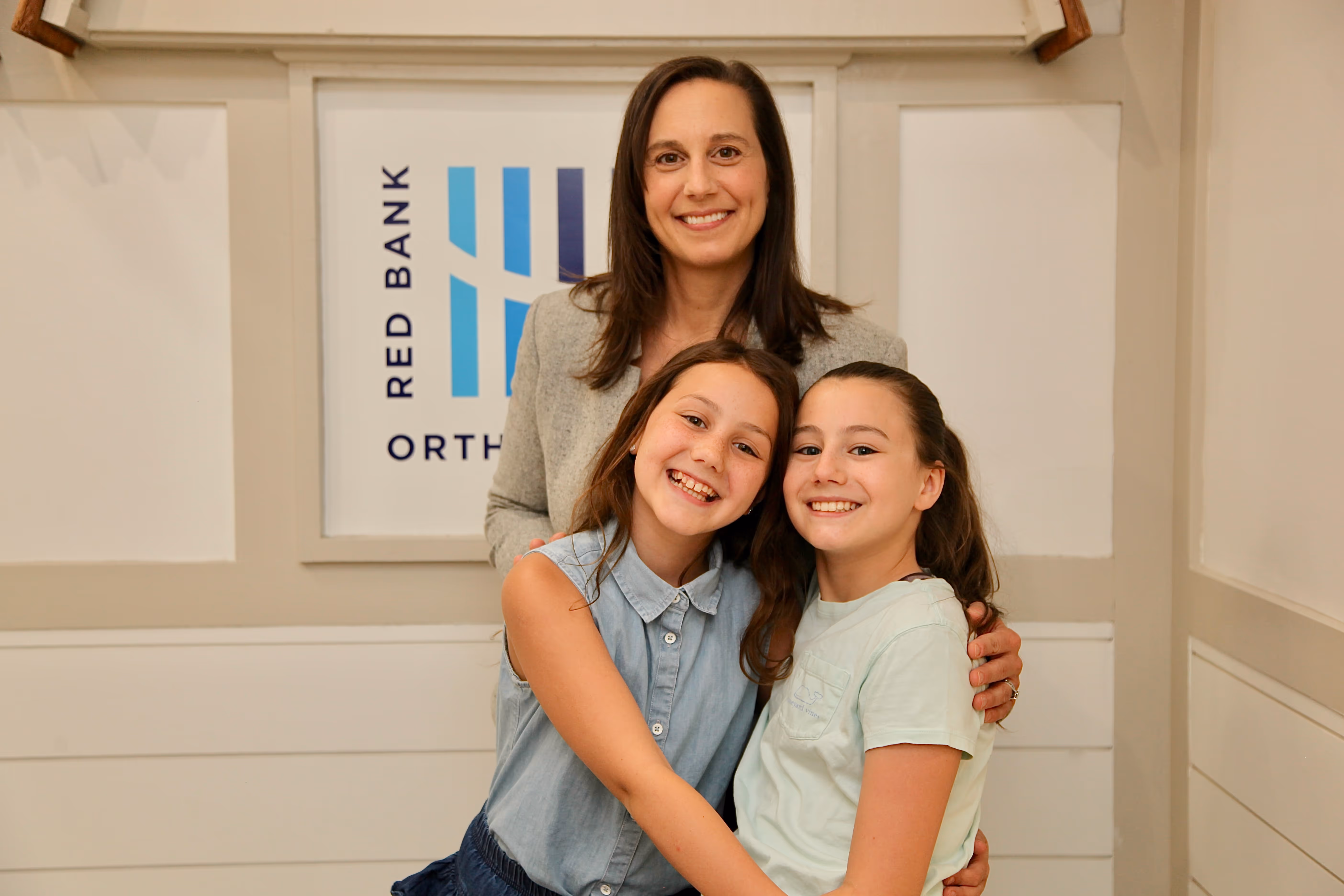 Six women in white sweatshirts and navy pants smiling inside a bright office reception area.