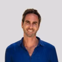 Smiling Thibault Henry with short brown hair wearing a blue shirt against a light gray background.