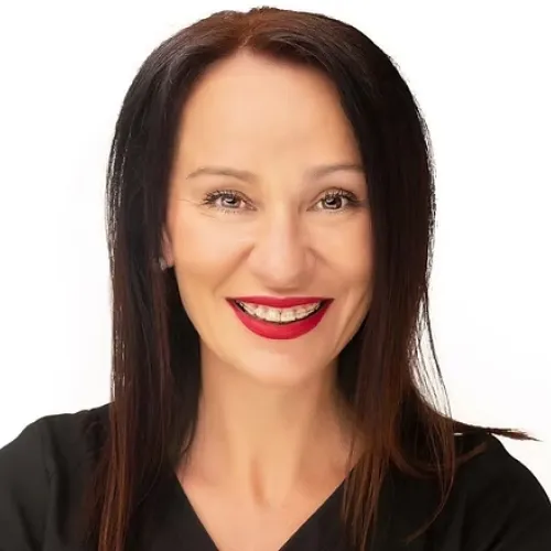 Smiling woman with long dark hair and red lipstick wearing a black top against a white background.