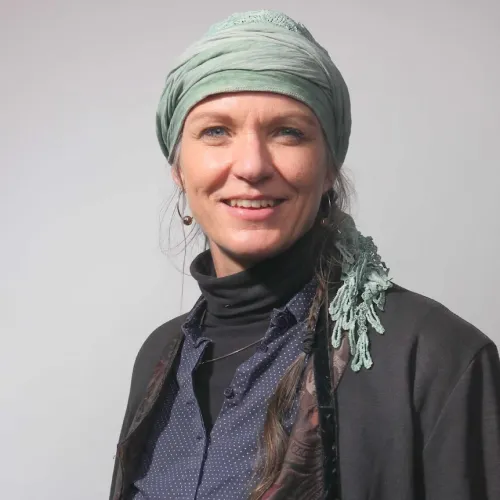 Smiling Pia Winberg wearing a light green headscarf and dark clothing against a plain gray background.