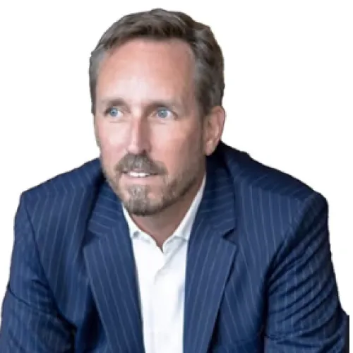 Man with short brown hair and beard wearing a blue pinstripe suit and white shirt, looking slightly to the side.