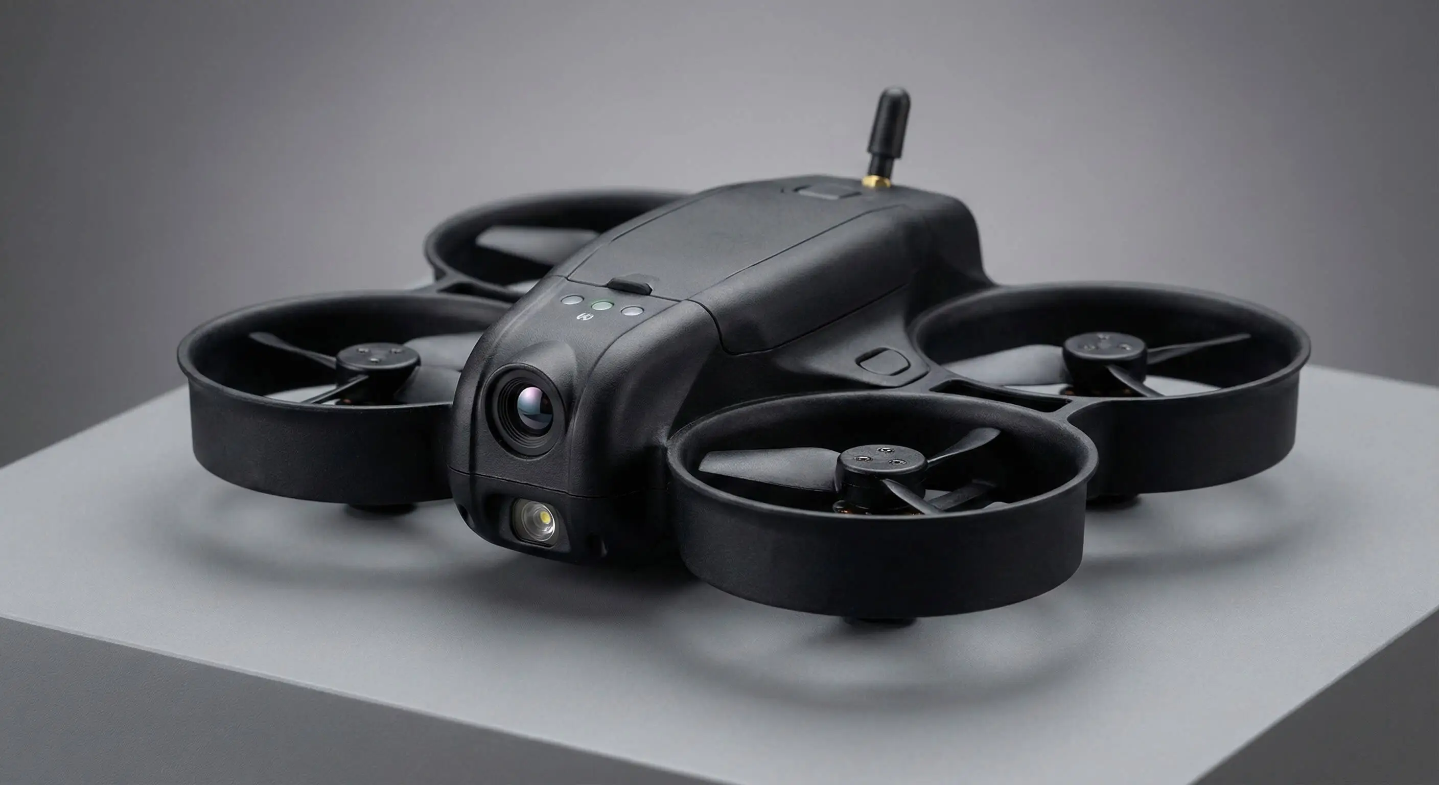 Compact black quadcopter drone with a front camera and four propellers on a gray surface.