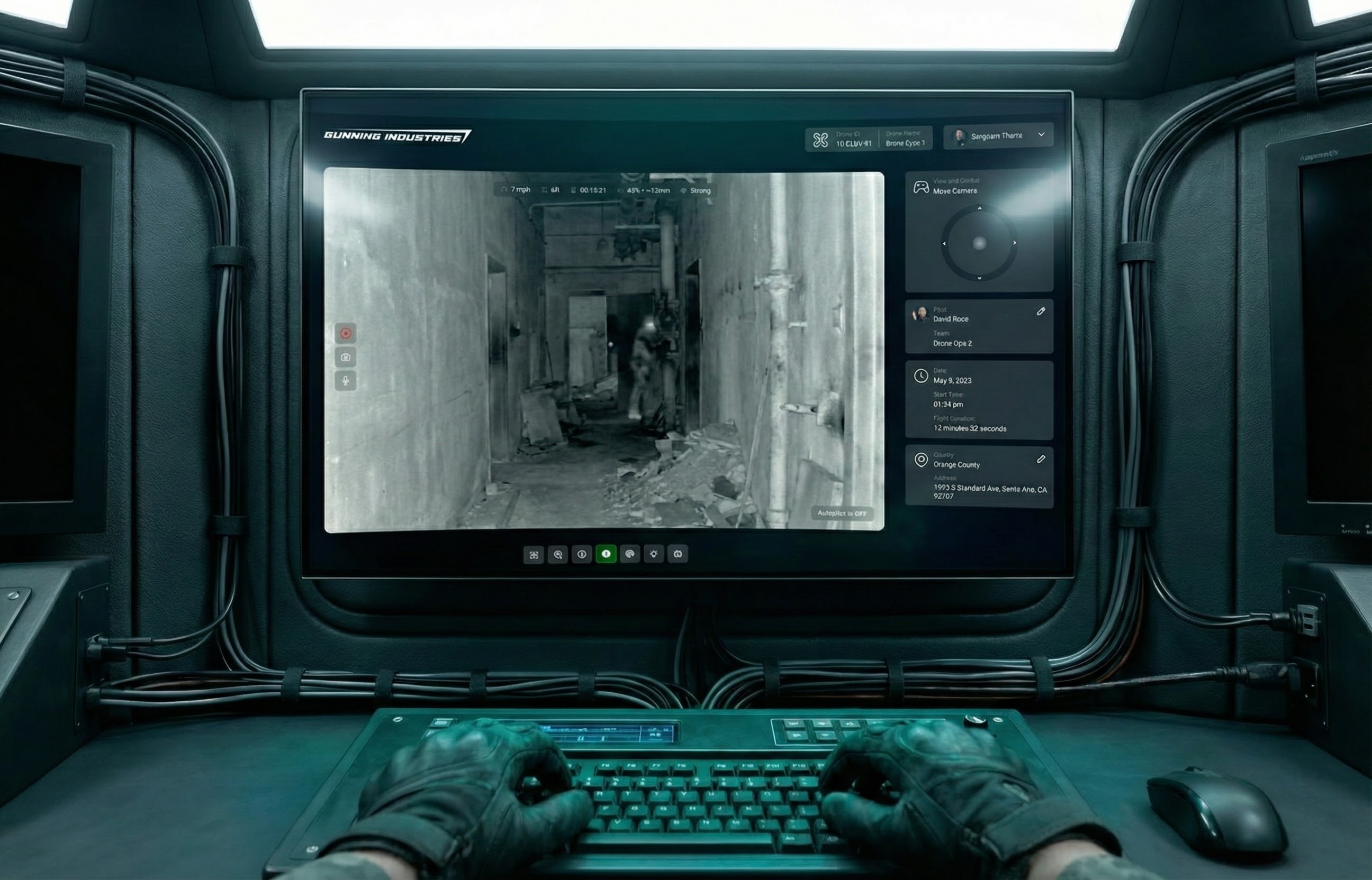 Gloved hands typing on a keyboard in front of a monitor showing a black and white drone camera feed inside a dilapidated building hallway.