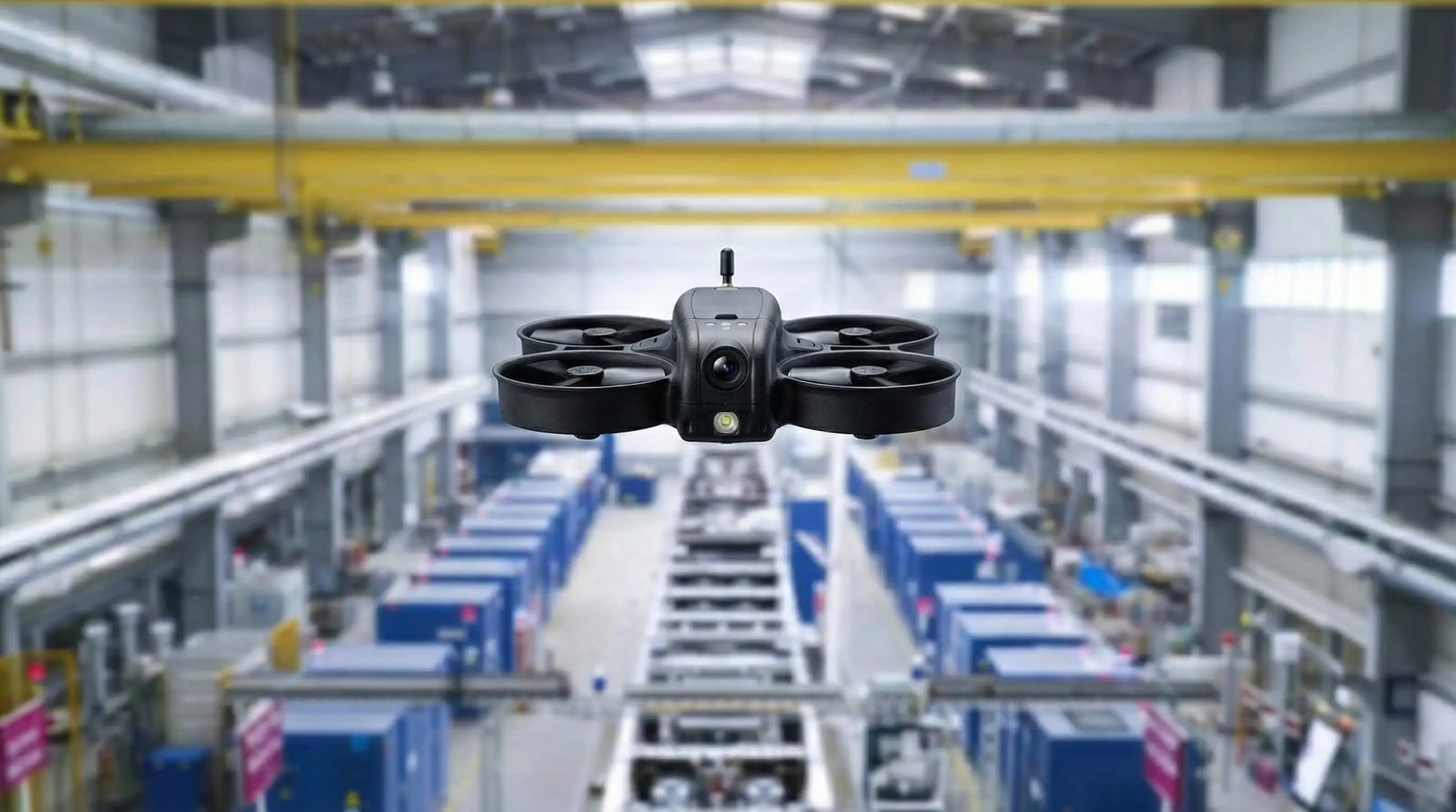 Black quadcopter drone hovering inside a large industrial warehouse.