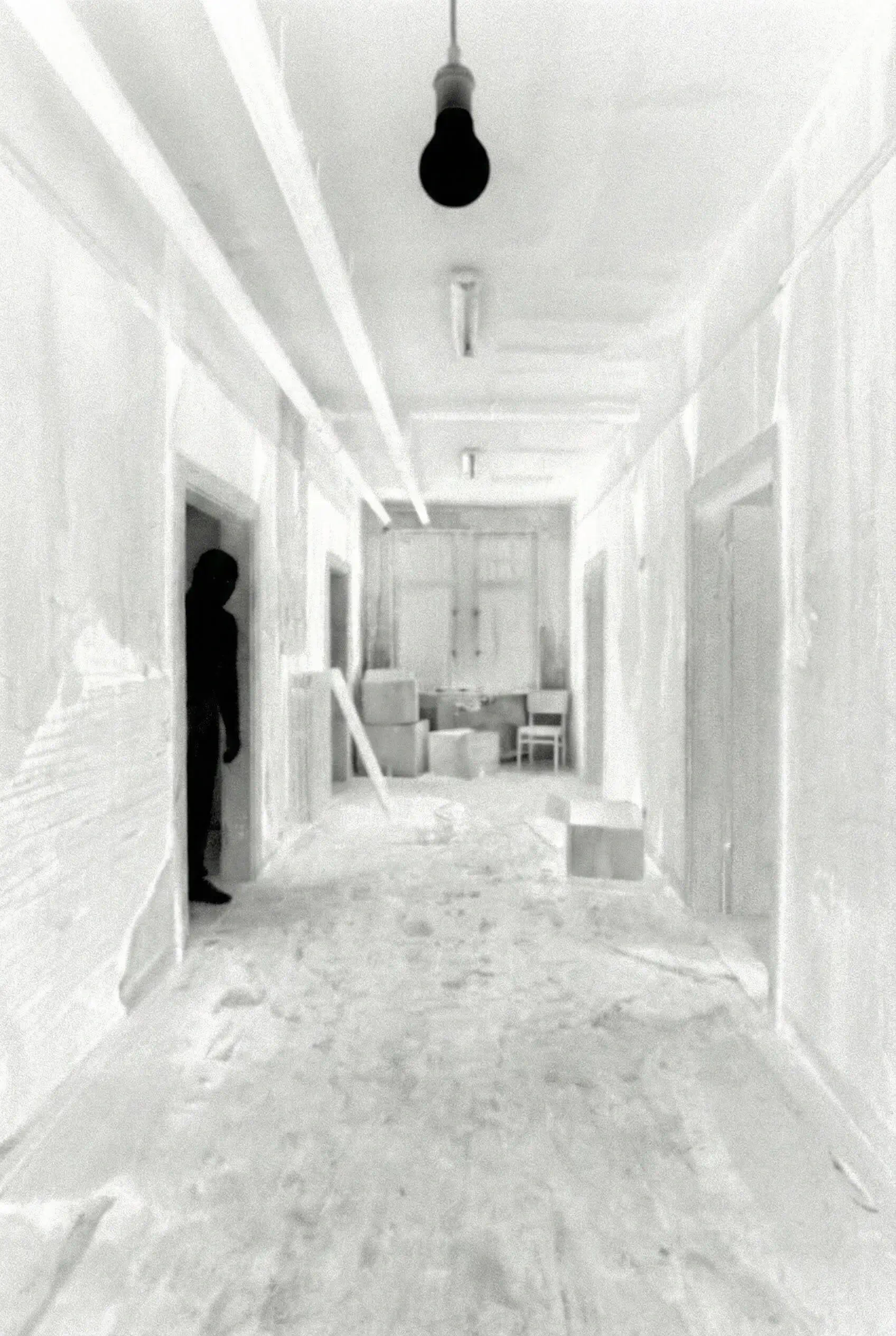 Deserted hallway with scattered boxes and a silhouette of a person standing in a doorway on the left.