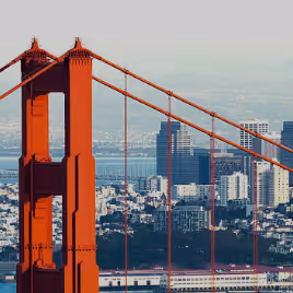 Close-up of the Golden Gate Bridge tower with San Francisco cityscape in the background.