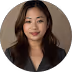 Portrait of a smiling young Asian woman with long dark hair wearing a dark blazer and dark top against a brown background.
